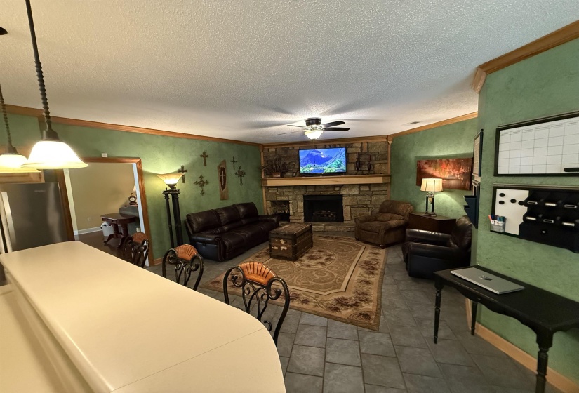 Tiled living area with crown molding, a fireplace, ceiling fan, and a textured ceiling