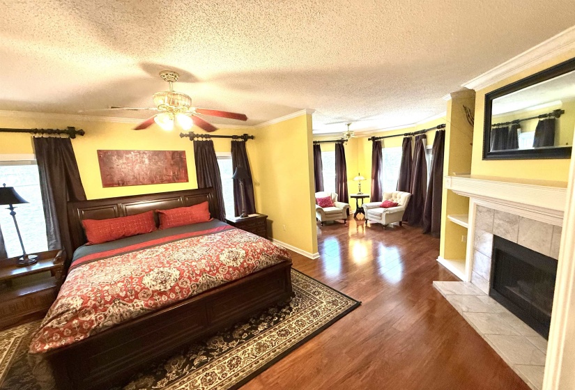 Bedroom featuring ornamental molding, a textured ceiling, wood finished floors, a ceiling fan, and a tiled fireplace