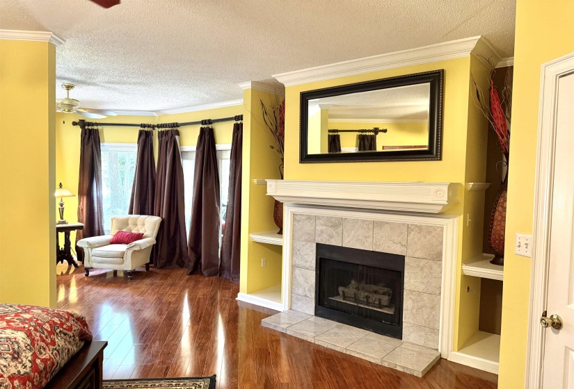 Living room with crown molding, wood finished floors, a textured ceiling, a fireplace, and ceiling fan