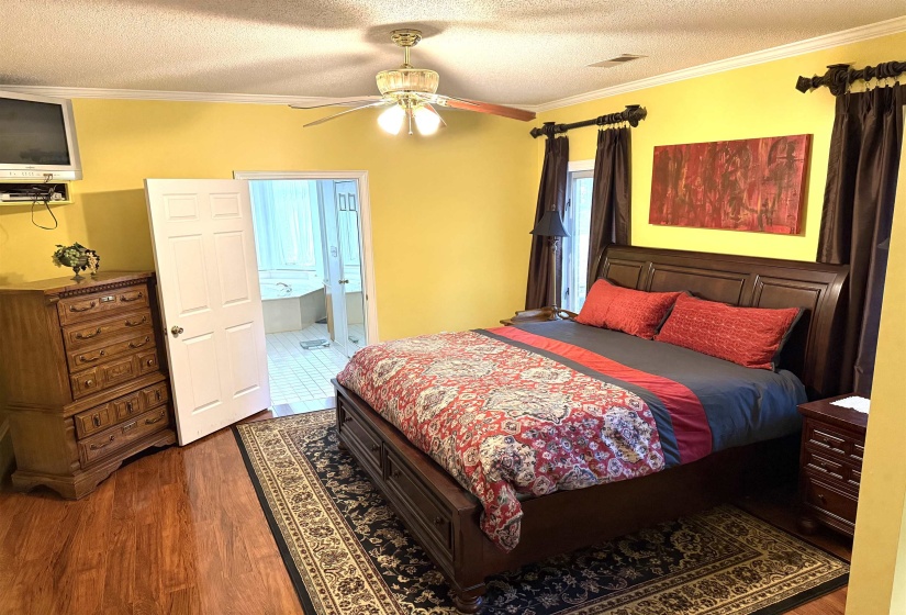 Bedroom with crown molding, a textured ceiling, dark wood-style floors, ensuite bathroom, and ceiling fan
