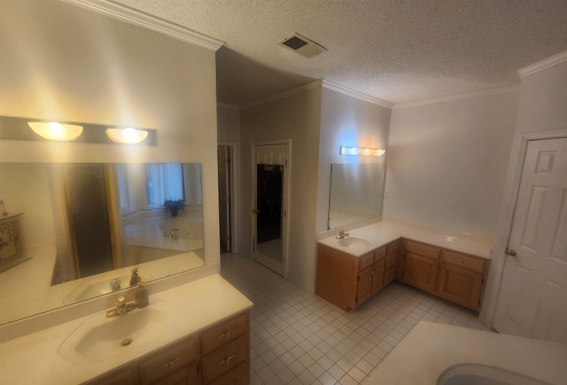 Full bathroom featuring a textured ceiling, two vanities, ornamental molding, light tile patterned floors, and a garden tub