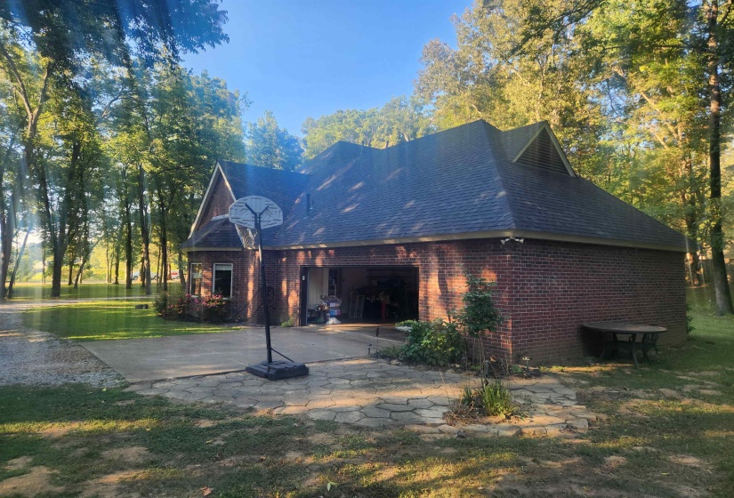 Back of house featuring brick siding, a patio area, roof with shingles, driveway, and a lawn
