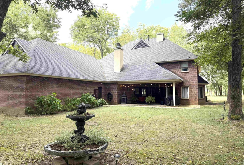 Back of house featuring a chimney, a lawn, a shingled roof, a patio area, and brick siding