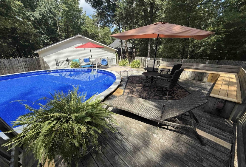 View of pool featuring a fenced backyard, view of wooded area, a deck, and outdoor dining space