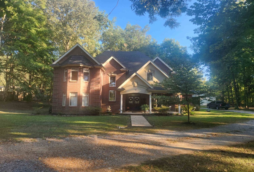 View of front of home with a front yard, brick siding, and gravel driveway