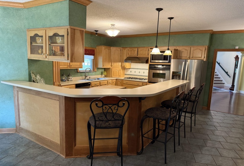 Kitchen with glass insert cabinets, light countertops, a breakfast bar, crown molding, and appliances with stainless steel finishes