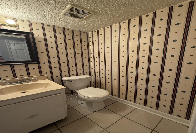 Bathroom with wallpapered walls, tile patterned flooring, vanity, and a textured ceiling