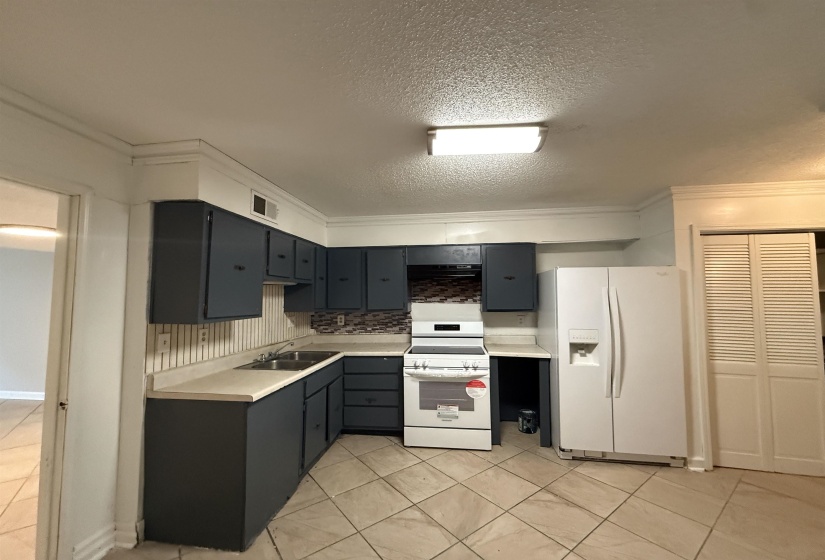 Kitchen with white appliances, light countertops, light tile patterned flooring, backsplash, and a textured ceiling