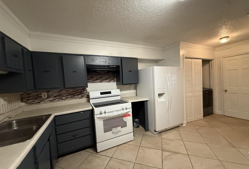 Kitchen featuring crown molding, backsplash, white appliances, a textured ceiling, and light countertops
