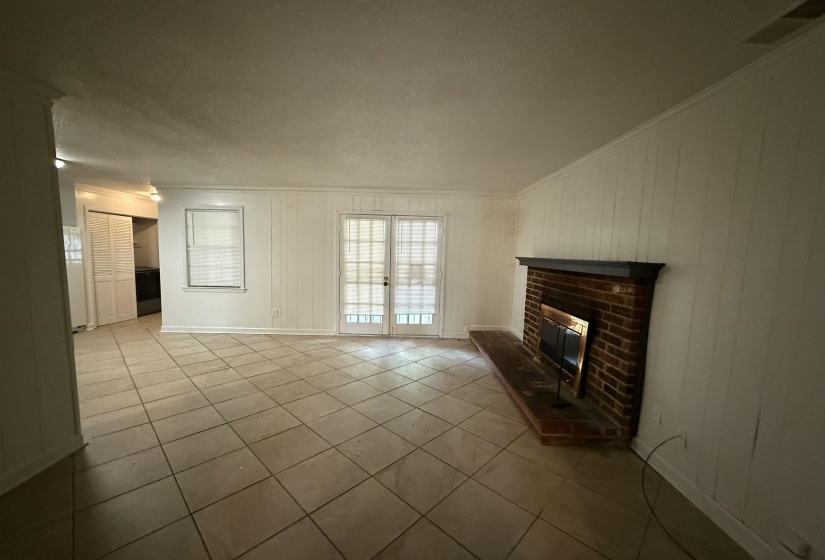 Unfurnished living room featuring ornamental molding, french doors, tile patterned flooring, a brick fireplace, and wood walls