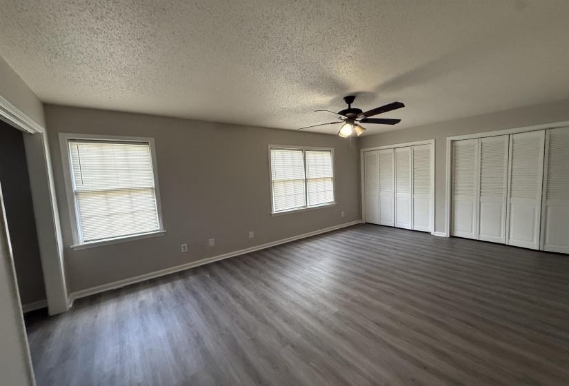 Unfurnished bedroom with two closets, dark wood-type flooring, ceiling fan, and a textured ceiling