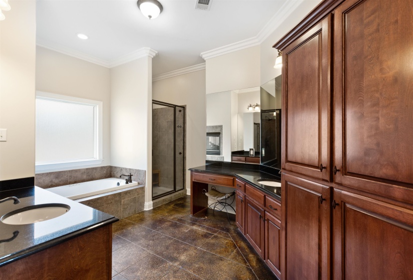 Primary Bathroom featuring stained concrete floors, a walk-in shower, jettted tub, crown molding, and dual vanities