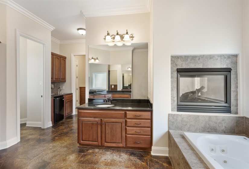 Primary Bathroom featuring stained concrete floors, a walk-in shower, jettted tub, crown molding, dual vanities, and see-thru fireplace for relaxation