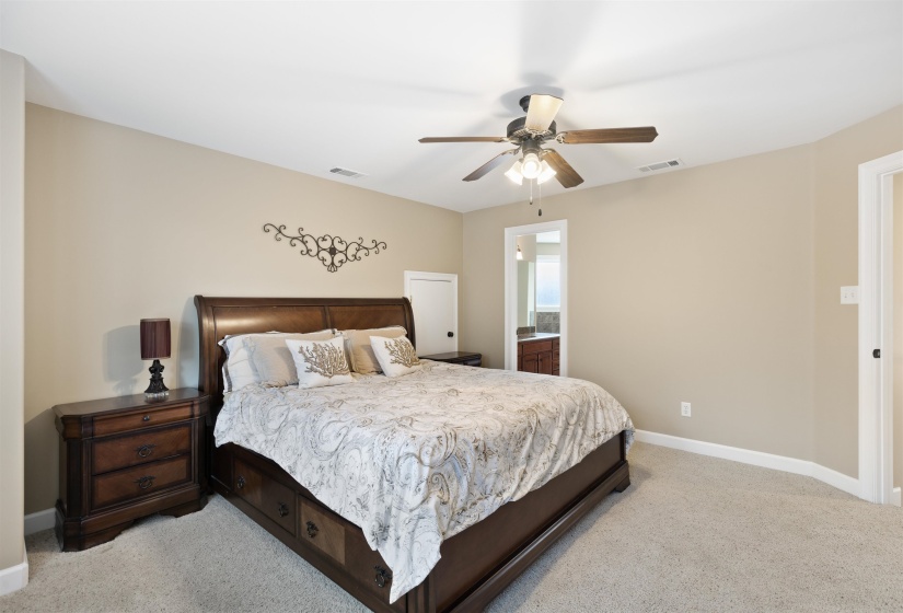 Bedroom with ceiling fan, light colored carpet, and connected bathroom