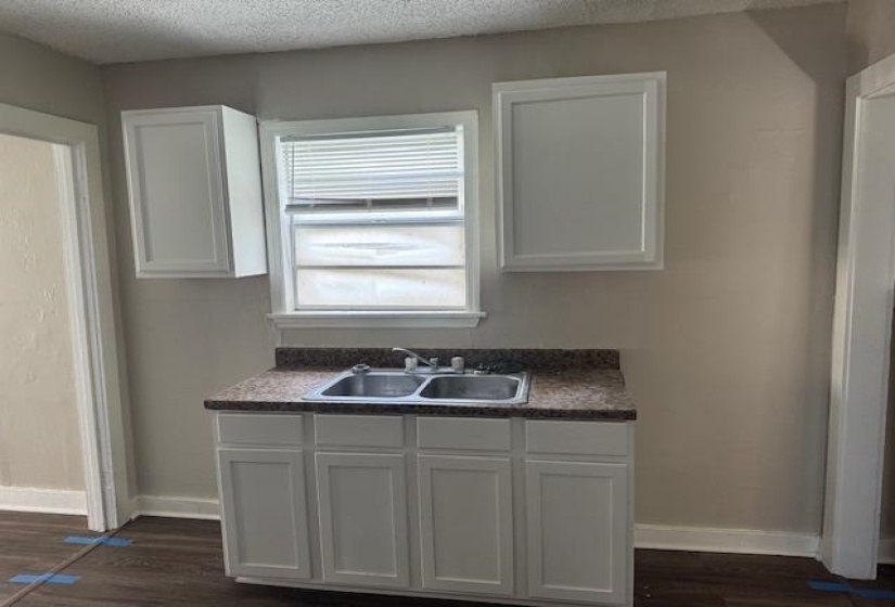 Kitchen with a sink, a textured ceiling, white cabinetry, and dark wood finished floors