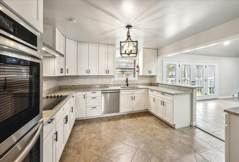 Kitchen with decorative light fixtures, white cabinetry, sink, stainless steel appliances, and light stone countertops