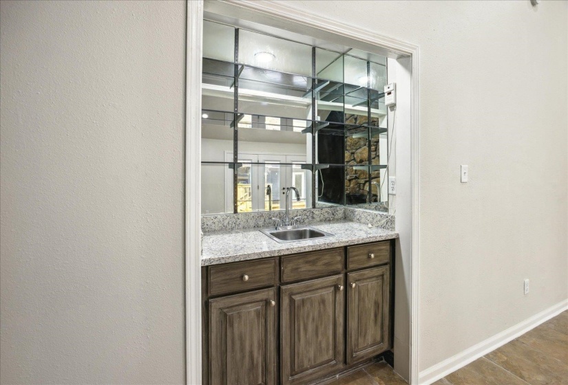 Bar featuring dark brown cabinetry, sink, and light stone counters