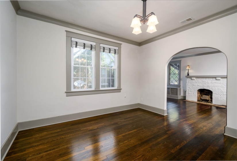 Unfurnished living room featuring arched walkways, ornamental molding, dark wood finished floors, a fireplace with raised hearth, and a chandelier