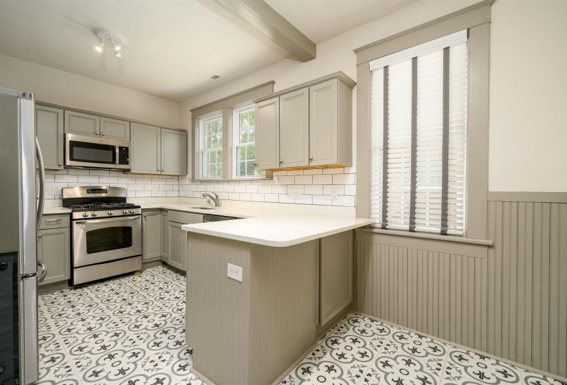 Kitchen with stainless steel appliances, tasteful backsplash, gray cabinetry, a peninsula, and wainscoting