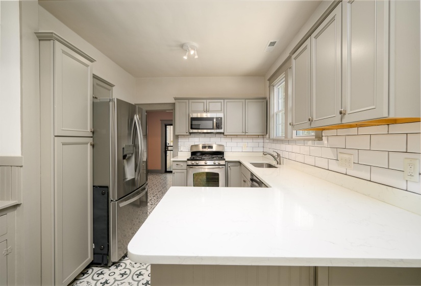 Kitchen with stainless steel appliances, a peninsula, decorative backsplash, gray cabinets, and light stone counters