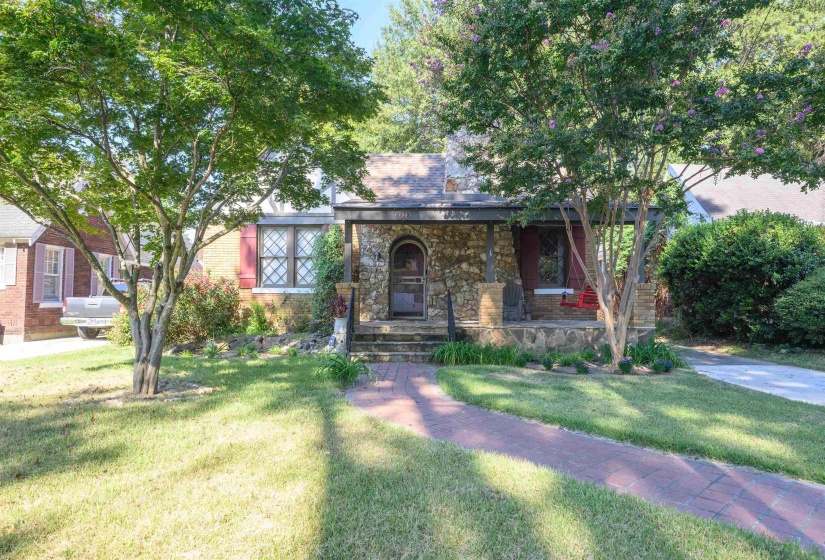 View of front facade with covered porch, brick siding, a front yard, and stone siding