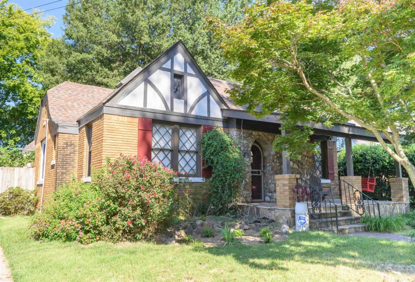 English style home featuring covered porch, a shingled roof, brick siding, and stone siding