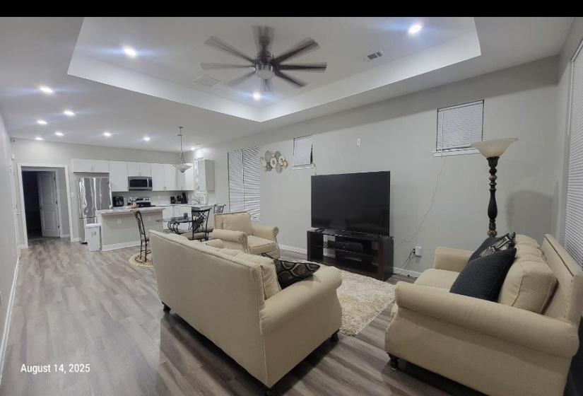 Living area featuring a raised ceiling, light wood-style flooring, ceiling fan, and recessed lighting