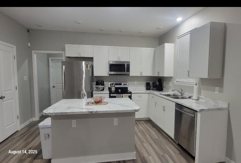 Kitchen featuring stainless steel appliances, white cabinetry, light wood finished floors, a center island, and recessed lighting