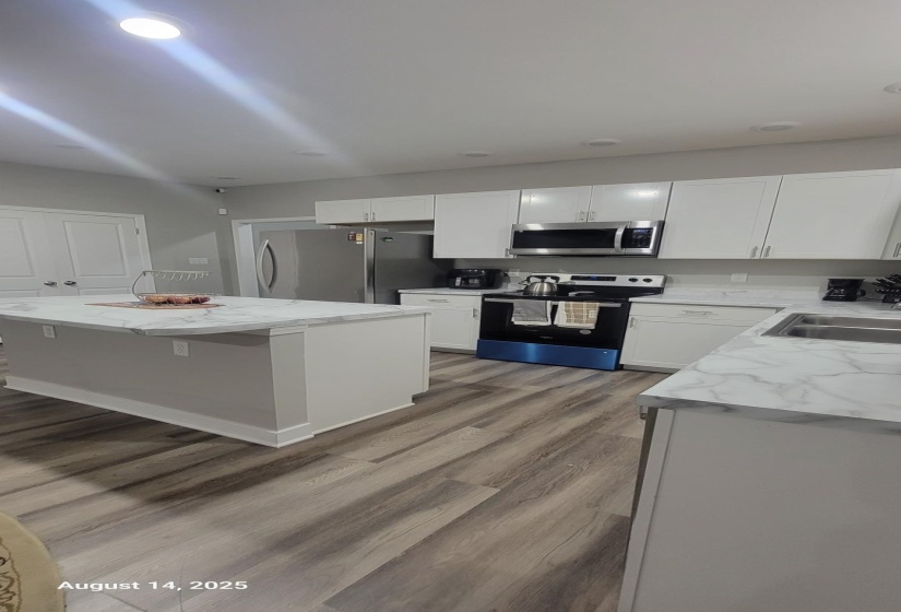 Kitchen featuring stainless steel appliances, white cabinets, light wood-style flooring, a kitchen island, and light stone counters