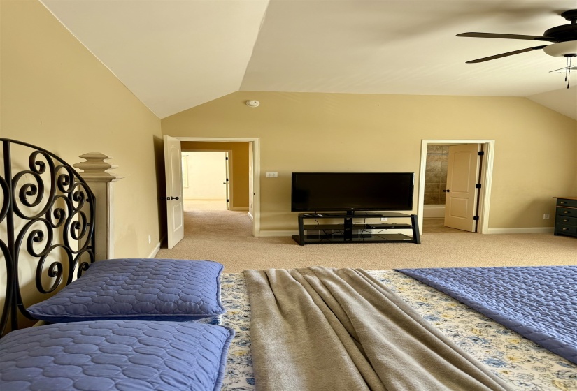 Bedroom with vaulted ceiling, light carpet, ensuite bathroom, and ceiling fan