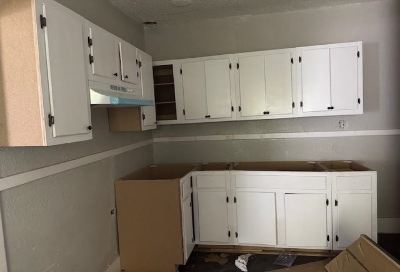 Kitchen with white cabinets, a textured ceiling, and under cabinet range hood