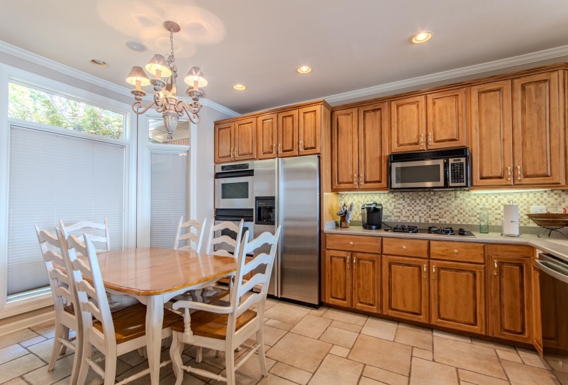 Kitchen with brown cabinetry, appliances with stainless steel finishes, backsplash, decorative light fixtures, and ornamental molding