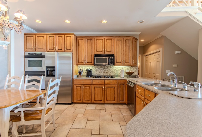 Kitchen featuring brown cabinets, stainless steel appliances, backsplash, recessed lighting, and ornamental molding