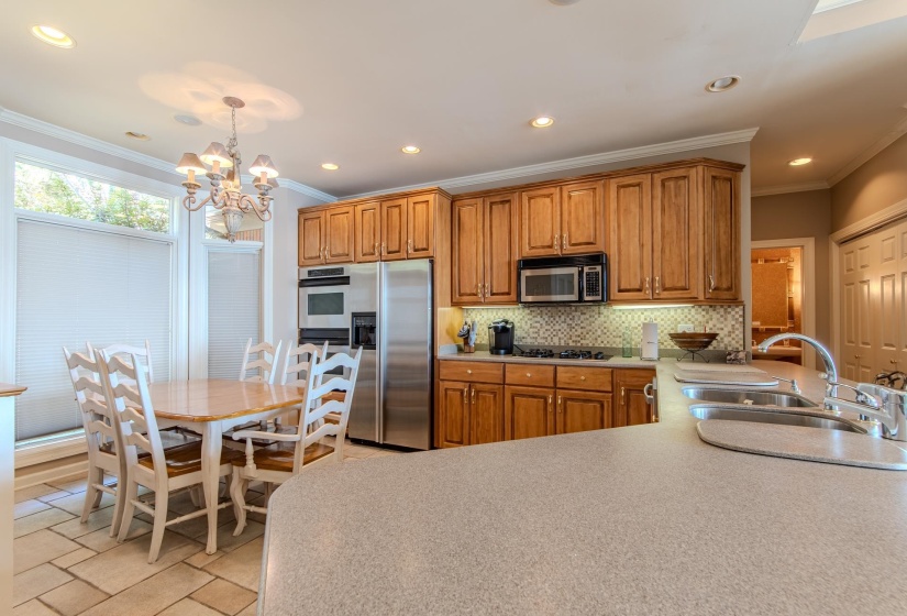 Kitchen with ornamental molding, decorative backsplash, brown cabinetry, light countertops, and recessed lighting