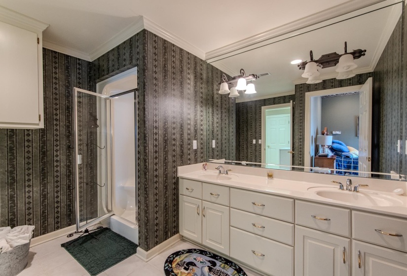 Ensuite bathroom featuring a shower stall, ornamental molding, double vanity, light tile patterned floors, and wallpapered walls