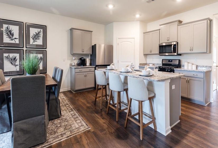 Kitchen featuring gray cabinetry, appliances with stainless steel finishes, dark wood-type flooring, a breakfast bar area, and an island with sink