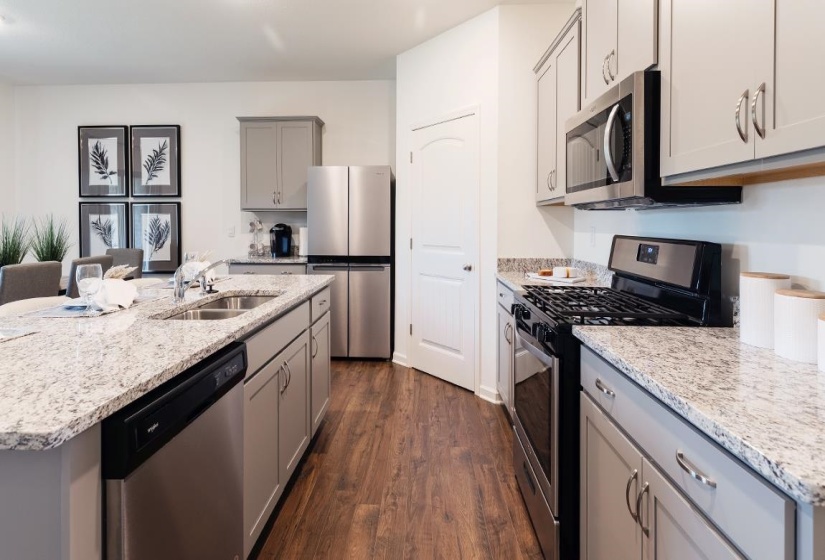 Kitchen featuring gray cabinets, appliances with stainless steel finishes, dark wood-style flooring, a kitchen island with sink, and light stone counters