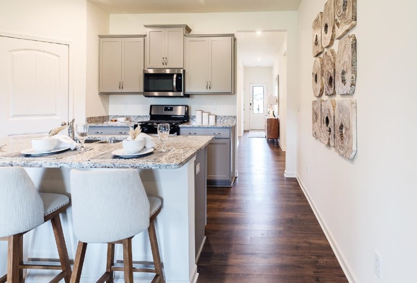 Kitchen with gray cabinetry, stainless steel appliances, dark wood-style flooring, light stone counters, and a kitchen bar