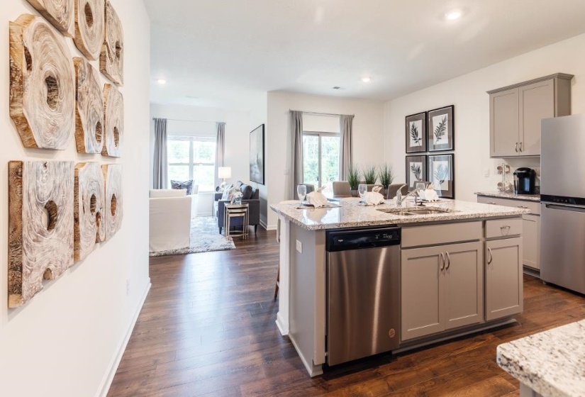 Kitchen with gray cabinets, appliances with stainless steel finishes, dark wood finished floors, light stone counters, and an island with sink