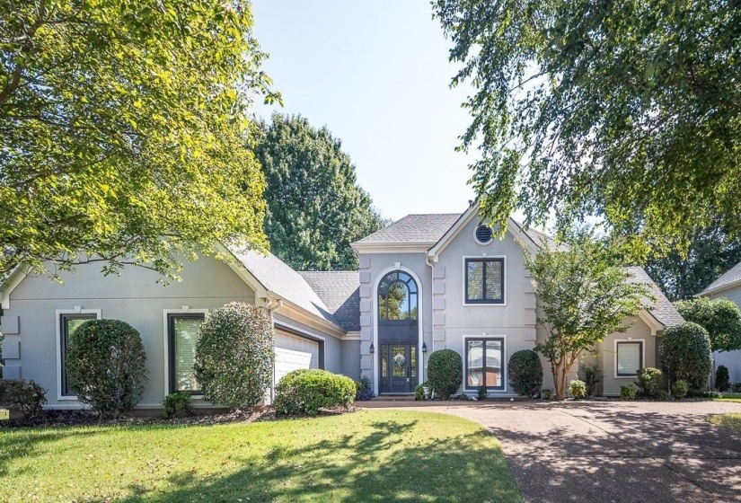 View of front facade with stucco siding, a front lawn, driveway, and roof with shingles