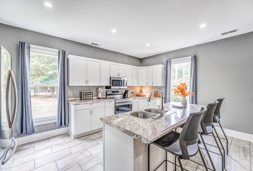 Kitchen featuring stainless steel appliances, white cabinetry, a kitchen breakfast bar, light countertops, and an island with sink