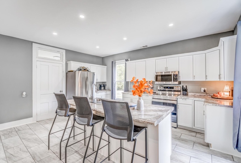 Kitchen with stainless steel appliances, an island with sink, a kitchen breakfast bar, white cabinets, and recessed lighting