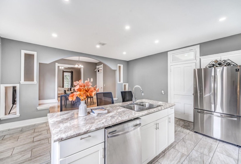 Kitchen with white cabinetry, stainless steel appliances, arched walkways, an island with sink, and recessed lighting