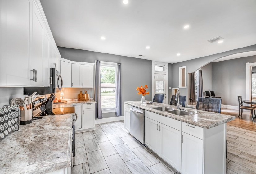 Kitchen featuring appliances with stainless steel finishes, arched walkways, white cabinetry, recessed lighting, and an island with sink