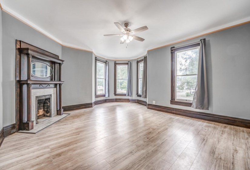 Unfurnished living room with crown molding, plenty of natural light, light wood-style floors, a fireplace, and a ceiling fan