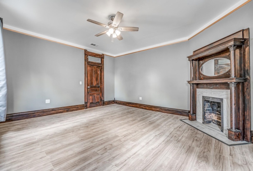 Unfurnished living room featuring ornamental molding, a ceiling fan, a fireplace, and wood finished floors
