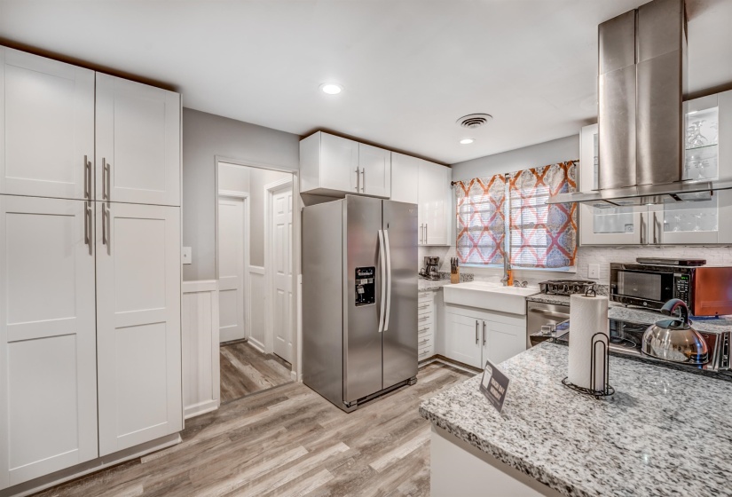Kitchen with white cabinets, light wood-type flooring, light stone counters, island exhaust hood, and stainless steel appliances