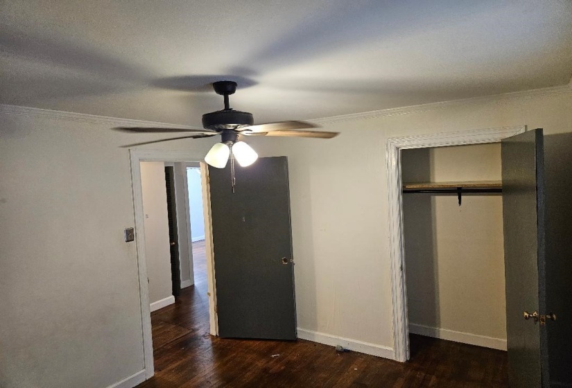 Unfurnished bedroom featuring ornamental molding, dark wood-type flooring, a closet, and ceiling fan