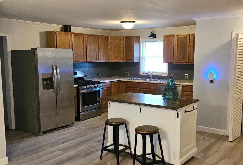 Kitchen featuring crown molding, dark countertops, stainless steel appliances, a kitchen breakfast bar, and light wood finished floors