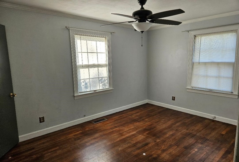 Empty room with crown molding, dark wood finished floors, and a ceiling fan